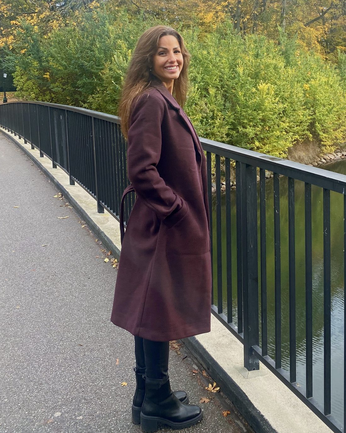 Cecilia Nord står på en bro i høstlandskap med gule og rustfargede trær