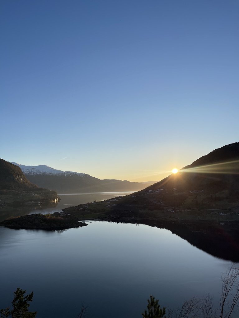 Solen stiger over fjellet ved Sognefjorden, og vannet ligger blankt og stille